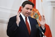 A photograph of Florida governor Ron DeSantis holding up his hands and speaking into a microphone.