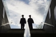 Two college graduates walk up a set of stairs, backlit with bright morning light.
