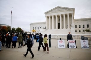 The scene in front of the Supreme Court Oct. 31, when the court heard arguments in two cases challenging race-conscious admissions in higher education: a lone opponent of affirmative action, with protest signs, stands next to a group of mostly young people  rallying in support of affirmative action. 