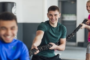 A point of view shot of a small multiethnic group of young men pulling on a rope at their local gym. They are wearing sports clothing and training in an indoor gym.
