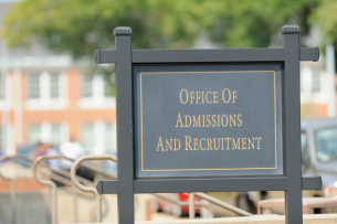 A black sign on a university campus that reads "Office of Admissions and Recruitment."