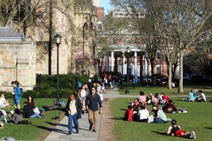 A crowd of people lounge on a campus green in front of a columned building facade