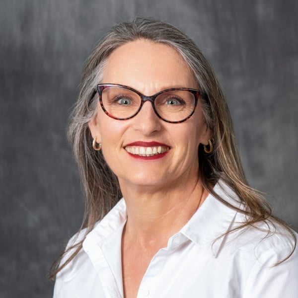 Deborah Dougherty, a light-skinned woman with brown hair streaked with gray. She is wearing glasses and a bright lipstick.