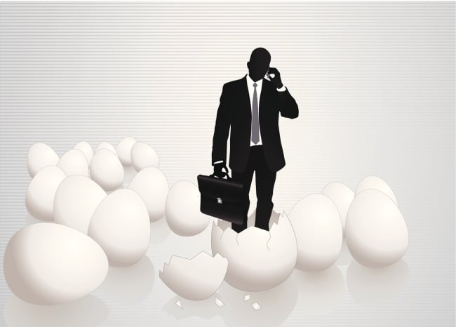 Dark man in suit and tie with briefcase stands on broken egg shells