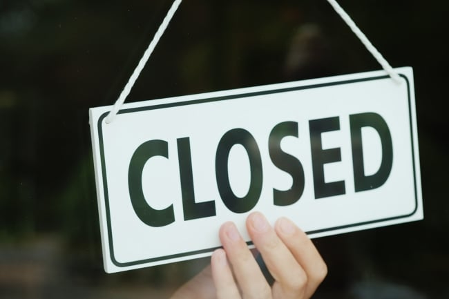 A hand can be seen adjusting a black and white sign that reads “CLOSED.”