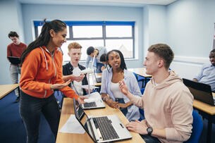 A young woman shows her classmates a 3-D wind turbine model in their engineering class. Both of the students are using a laptop.