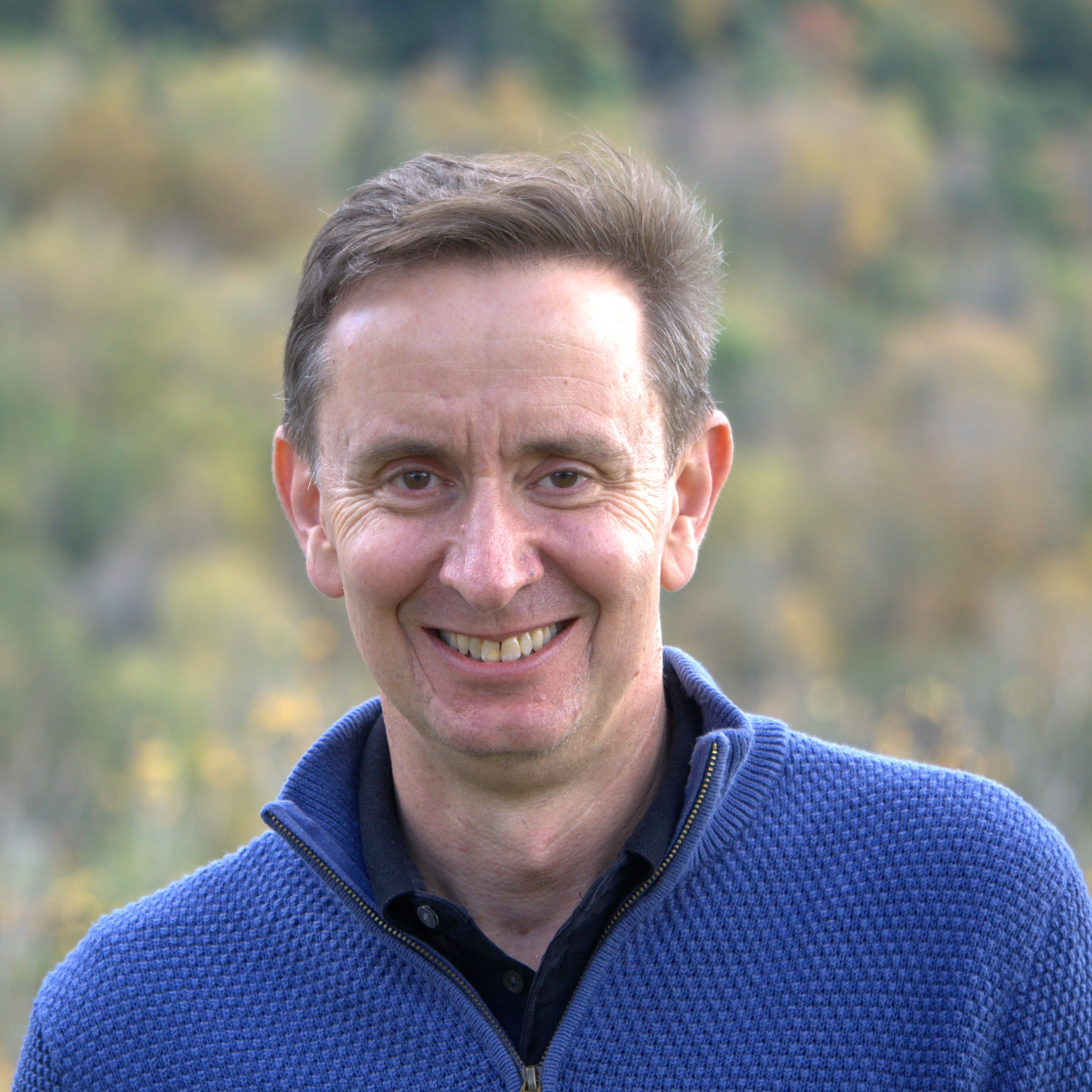 Peter Felten smiles for a headshot wearing a blue polo outdoors