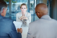 Anxious woman looks at two men interviewers with their backs to the viewer