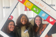 Three first-generation students smile at a Rutgers University first-gen event with a photo-booth frame