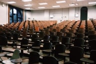 An empty lecture hall full of brown chairs.