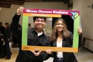 Two students pose in black-and-white business attire inside a photo frame that says Mason Chooses Kindness