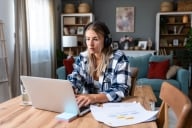 Happy woman wearing wireless headphones working on laptop at home office