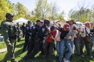 A photo of police officers in helmets trying to break up a group of protesters who have locked arms with one another.