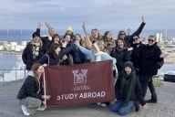 A group of students and several professors pose with a College of Charleston flag on the roof a waste-to-energy plant in Denmark.