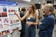 A student researcher discusses her poster with a faculty member