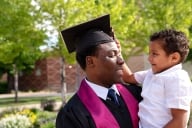 A Black man in a graduation cap holds a toddler