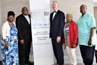 Four alumni stand with Lincoln University president John Moseley in front of a sign that reads "Welcome alumni, family and friends."