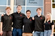 A group of Gonzaga students smile for a photo wearing matching black polos with a Gonzaga Sport Consulting Group logo