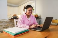 A student works on her laptop wearing headphones and smiling.
