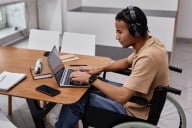 Portrait of young Black man with disability using laptop in college library and wearing headphones