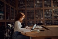 Young woman sits in library writing at a computer 