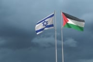 Israeli and Palestinian flags wave on two flagpoles next to one another.
