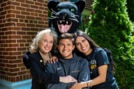 Three people pose for a photo with a panther mascot above them