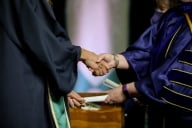 An unidentified student shakes the hand of a dean at graduation, accepting a diploma