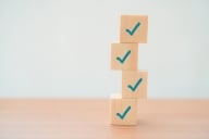 A stack of four wooden blocks, each with a blue checkmark, illustrating a checklist concept.