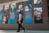 A student wearing a kippah and tzitzit, traditional Jewish fringes, walks in front of a brick academic building at Yeshiva University.