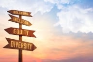 An image of a wooden signpost against the backdrop of a pink sunrise or sunset. The signpost has four signs, pointing in varied directions, that read "Belonging," "Inclusion," "Equity" and "Diversity."