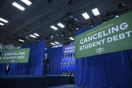 President Biden walks on a stage flanked by two signs that say "Canceling Student Debt" in white text.