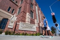 A student in a blue shirt walks past a brick campus building