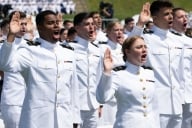 Graduate cadets in white uniforms salute in a crowd