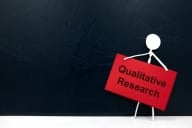 A drawing of a white stick figure holding a red sign that reads "Qualitative Research" against a solid black background.