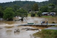 A few people stand on the edge of a washed-out road, surrounded by water.