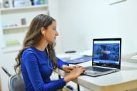 A graduate student completes coursework on her computer while wearing headphones