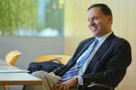 Ron Liebowitz sits in a chair in a navy suit, white shirt and blue striped tie