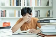 A male student holds his hand over his face as he struggles with academic work