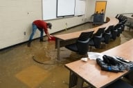 Volunteer scoops floodwater in classroom