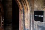 A sign reading "ADMISSIONS" hangs next to an archway on a stone building.