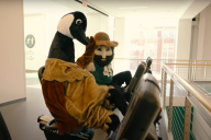 A goose and a gold miner, both mascot costumes, high-five while working on elliptical machines.