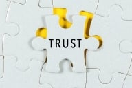 Puzzle piece fitting into larger puzzle board, with word "trust" on it