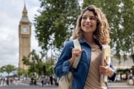 Happy woman studying English in London and walking down the street carrying notebooks while smiling