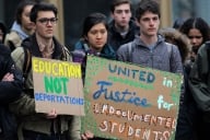 Three students stand with signs that read "education not deportation" and "united in justice for undocumented students."