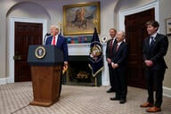 Oracle co-founder Larry Ellison, SoftBank CEO Masayoshi Son and OpenAI CEO Sam Altman joined President Trump for a White House announcement of a new artificial intelligence initiative Jan. 21. President Trump speaks at a lectern while the three tech executives are lined up in a row to his left.