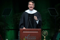 A photograph of Virginia governor Glenn Youngkin, in academic robes, speaking at a lectern with George Mason written on it.