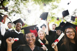 A group of about eight happy graduates, wearing caps and gowns and clutching diplomas while grinning at the camera.