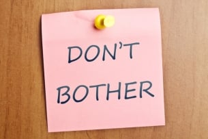 The words "Don't bother" written on a pink note tacked to a wooden door.