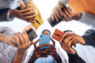 Students are gathered in a circle, all using their cellphones and looking down at the devices.